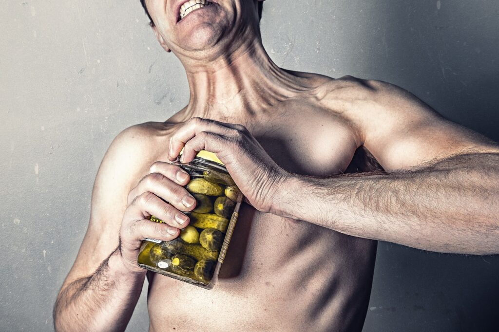 A shirtless man grips a jar of pickles